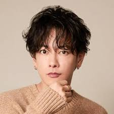 佐藤健のビジュアル。茶色のニットを着ていて、髪型はパーマがかかっている。